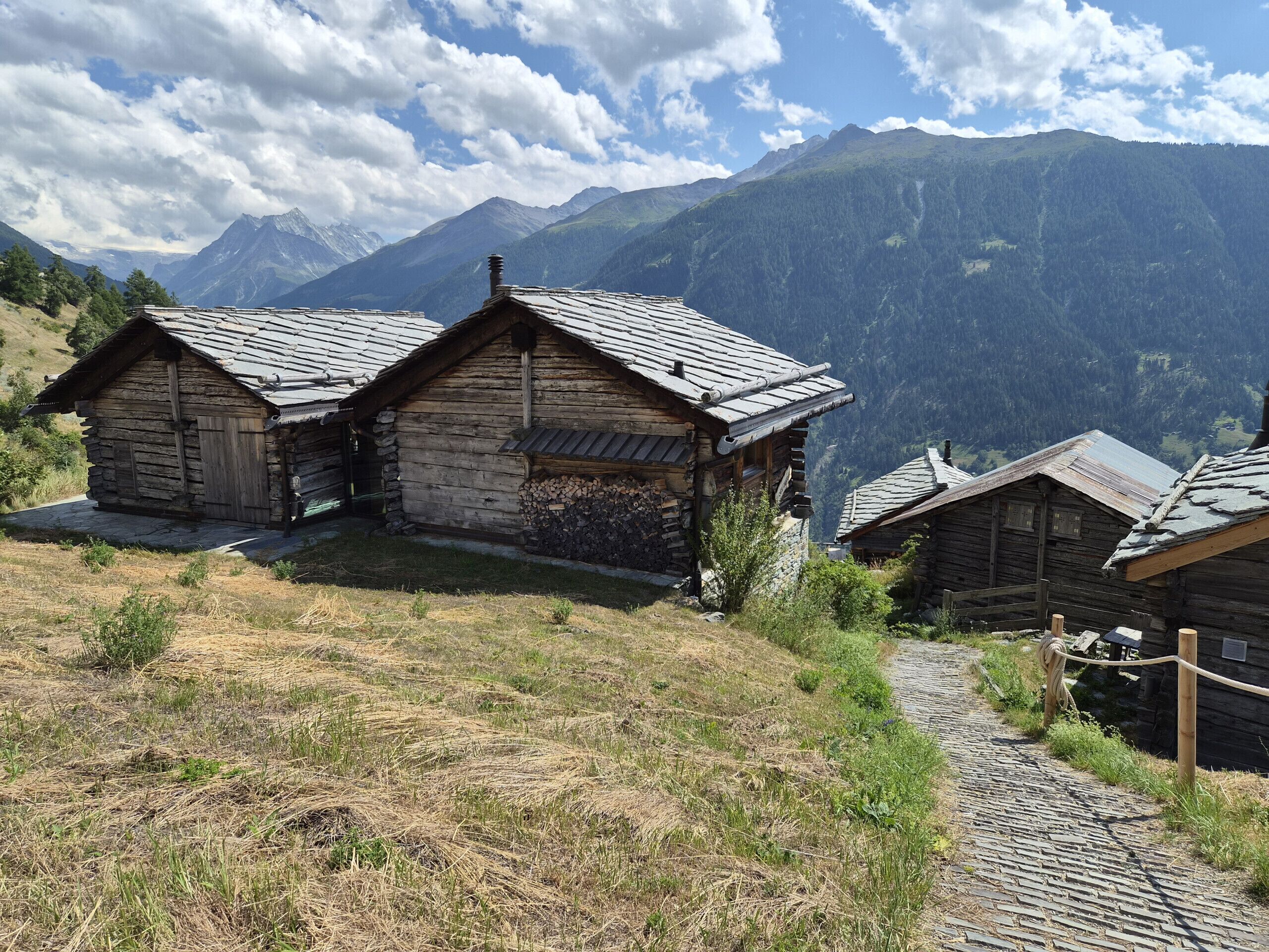 A row of rustic wooden cabins with sloped roofs, situated on a hillside with a mountain backdrop.