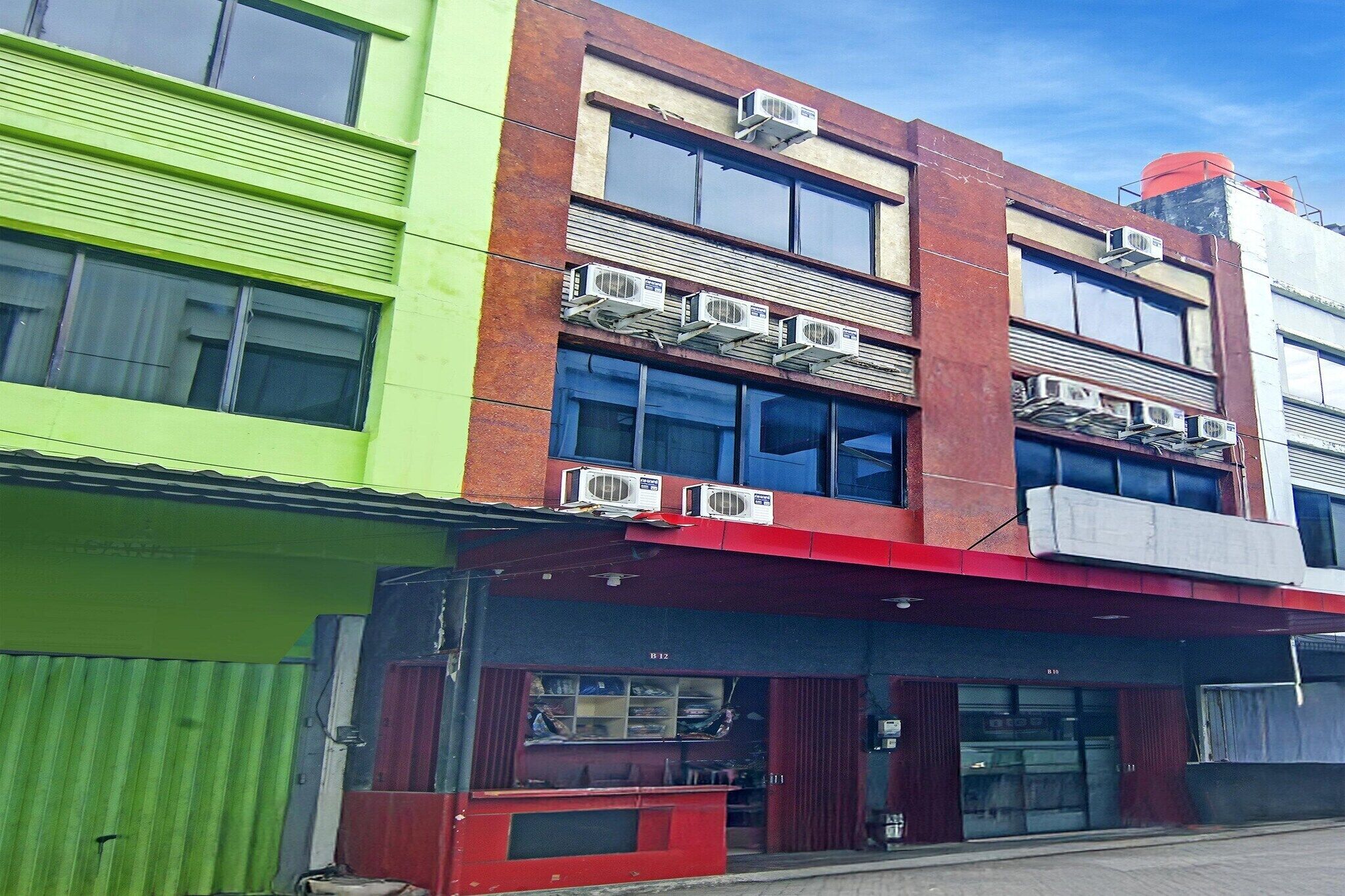 Un immeuble à plusieurs étages, doté de climatiseurs installés à l’extérieur, d’une devanture avec un auvent rouge et d’une façade verte.