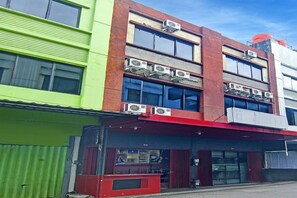 A multi-story building with air conditioning units on the exterior, a storefront with a red awning, and a green facade.