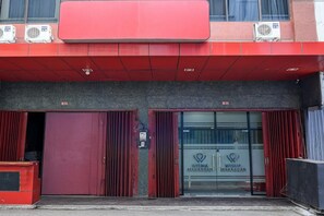 Entrada de un edificio con dos puertas rojas, identificadas con las etiquetas B12 y B10, y un letrero que dice WISMA MAKASSAR.