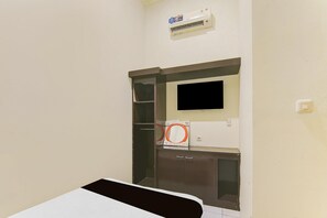 A room with a bed, a television mounted on the wall, and an air conditioning unit above it.