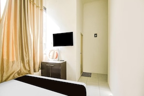 A hotel room with a bed, a television mounted on the wall, a small table with a remote control, and a shower area.