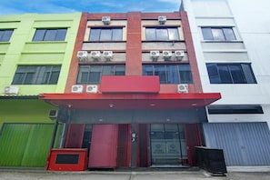 A multi-story building with a red awning, air conditioning units, and a green and white facade.