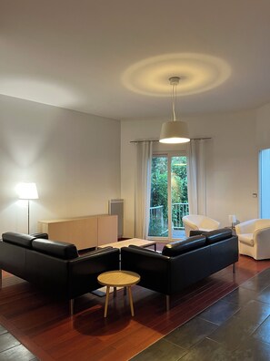 A modern living room with a sofa set, a round wooden table, and a hanging light fixture. - Family home 20 minutes from Paris (Palaiseau)