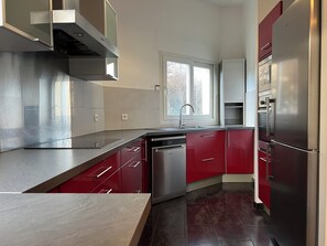 A modern kitchen with stainless steel appliances, red cabinetry, and a window providing natural light. - Family home 20 minutes from Paris (Palaiseau)