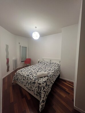 A bedroom with a bed, a red chair, a window with blinds, and a hanging light fixture. - Family home 20 minutes from Paris (Palaiseau)