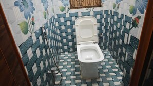 A small bathroom with a toilet, a shower area, and a tiled floor with a floral pattern. - Khushi Home Stay (Varanasi)