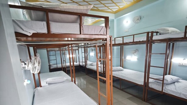 A dormitory room with bunk beds, a fan, and a tiled floor. - Khushi Home Stay (Varanasi)