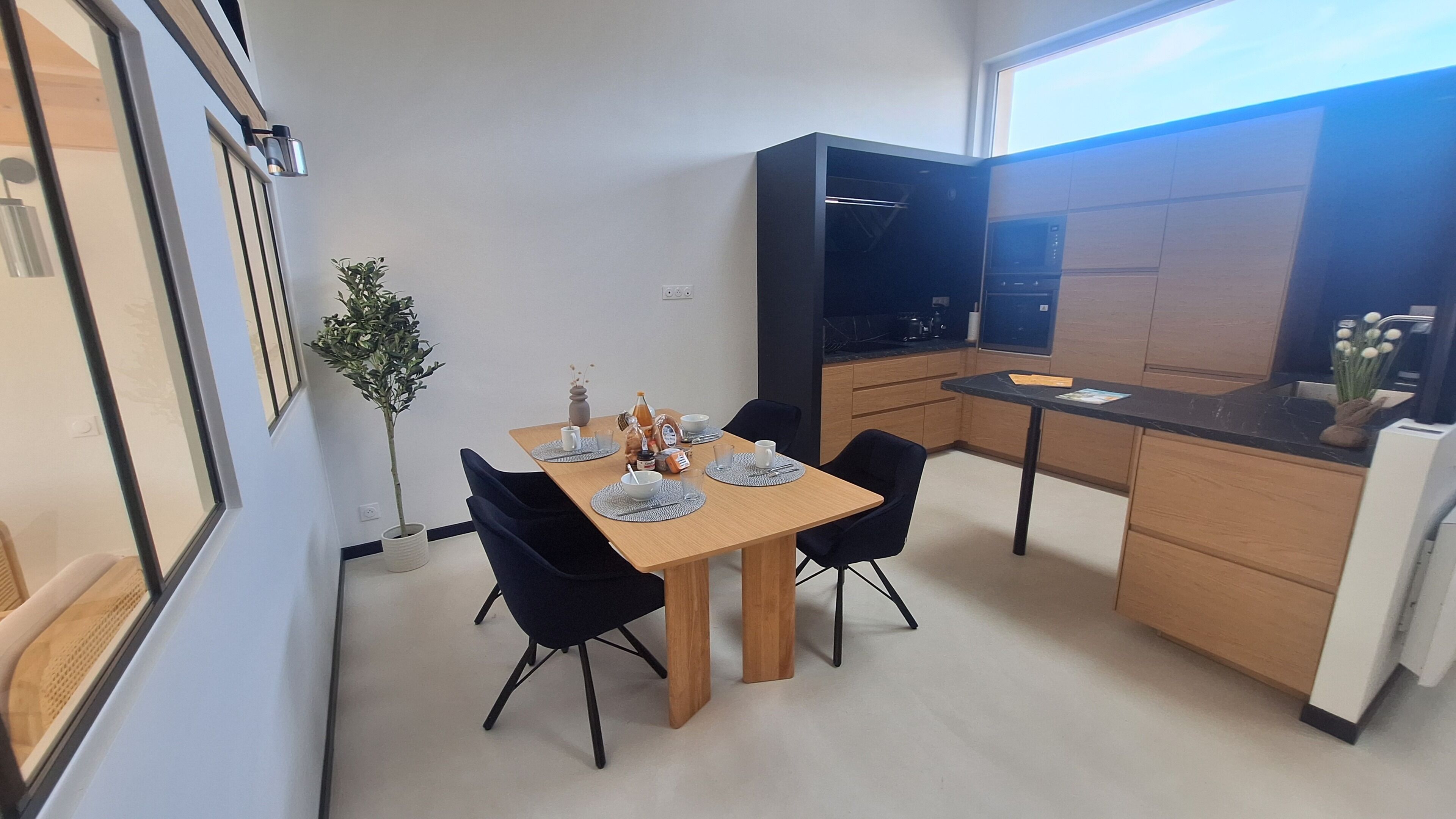 Eine moderne Küche mit Essbereich, ausgestattet mit einem Holztisch, schwarzen Stühlen und einem Blumentopf.