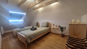 Ein Schlafzimmer mit zwei Betten, einem Oberlicht, Nachttischen, einer Holzbank und einem Topfpflanzen.