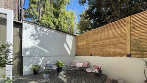 Eine Terrasse mit Gartenmöbeln, einem Holzzaun und Blumentöpfen.