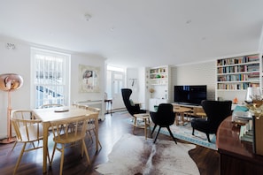 Una sala de estar moderna con comedor, televisor, estanterías y una escalera.