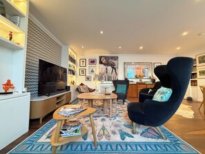 A modern living room with a dark blue armchair, a wooden coffee table, and a TV on a white cabinet. - Beautiful 2BDR Home Right by Regents Park (Greater London)