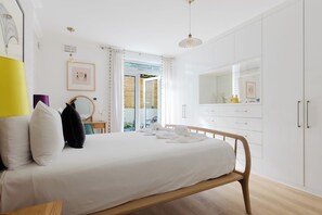 A bedroom with a bed, a bedside table, a mirror, a wardrobe, and a window with curtains. - Beautiful 2BDR Home Right by Regents Park (Greater London)