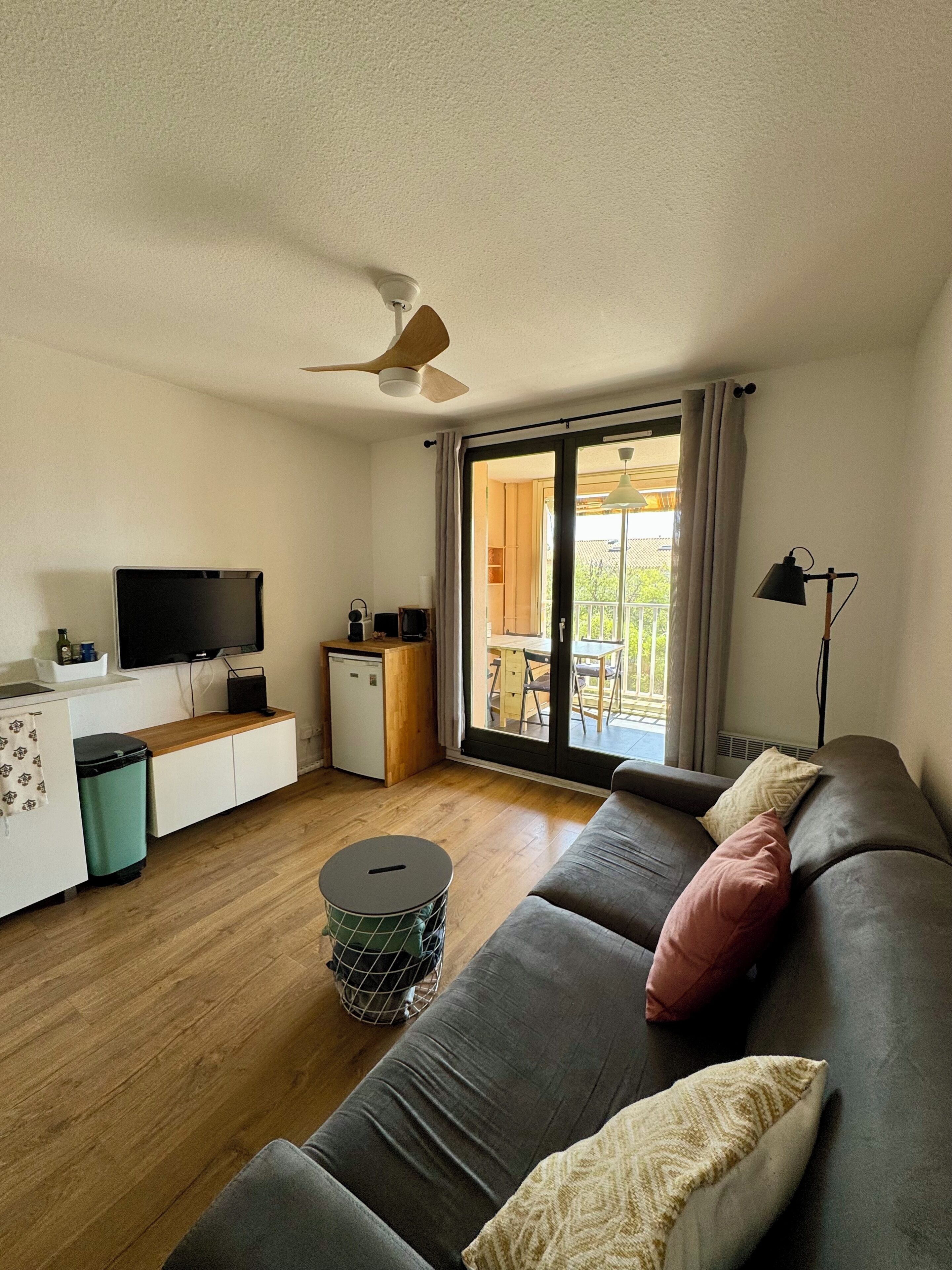 A compact living space with a sofa, a television, a small kitchenette, and a sliding glass door leading to an outdoor area.