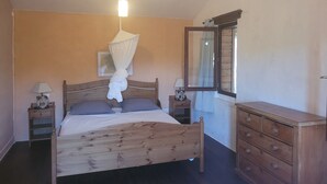 A bedroom with a wooden bed, bedside lamps, a nightstand, a wooden dresser, a mirror, and a hanging canopy.