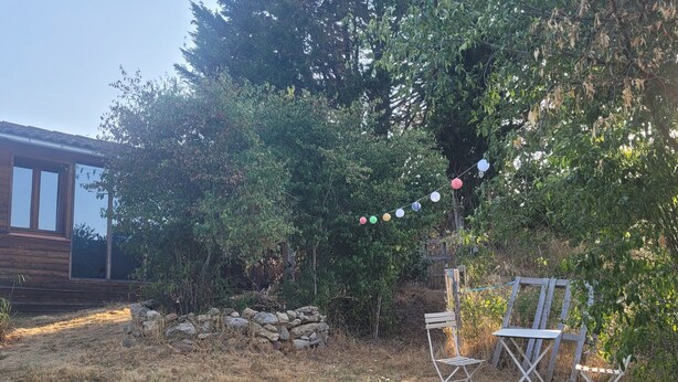 A backyard with a wooden deck, a stone wall, and a string of colorful lights.