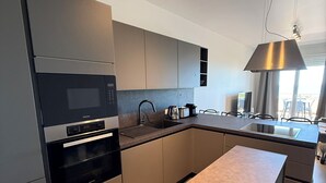 A modern kitchen with built-in appliances, a central island, and a dining area with chairs. - Brand-New Sea View in Vasto Marina with Parking (Marina di Vasto)