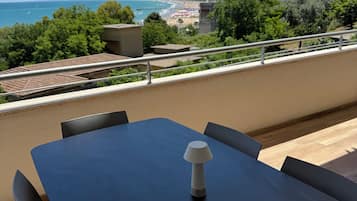 Un balcon avec une table et des chaises, offrant une vue sur la plage et l’océan.