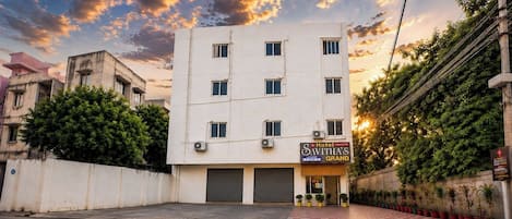 A hotel building with a sign for 'Savitha's Grand' and a row of potted plants in front.