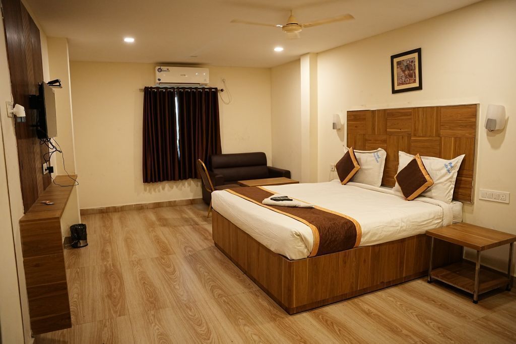 Habitación de hotel con una cama de madera, una silla, una mesita pequeña, un equipo de aire acondicionado y un ventilador de techo.