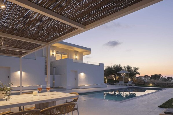 A modern outdoor pool area with a covered seating area and a stone wall in the background.