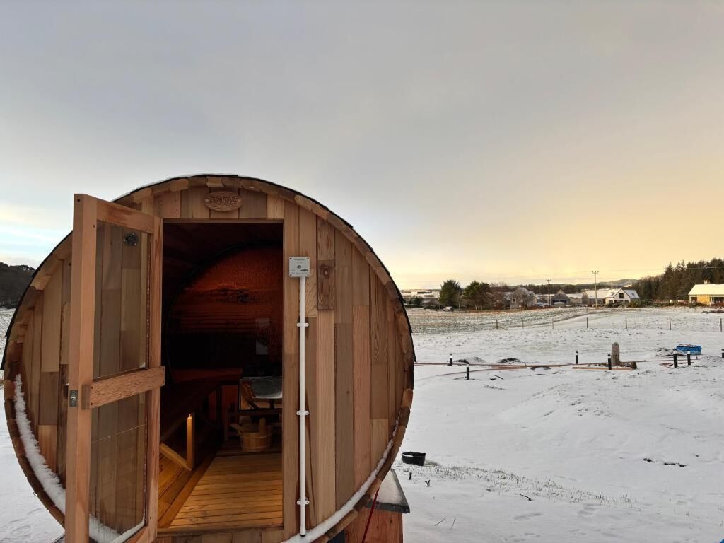 Une structure en bois avec une porte ouverte, un banc à l’intérieur et un paysage enneigé à l’extérieur.