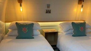 Habitación de hotel con dos camas, cada una con una almohada y una toalla doblada. Hay una mesita de noche entre las camas.