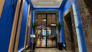 Vestíbulo de hotel con una decoración azul y blanca, suelo de mármol y una entrada de cristal que da al comedor.