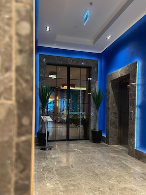 A hotel lobby with a glass door entrance, a reception desk, and a digital elevator display. - Axis Hotel (Trabzon)