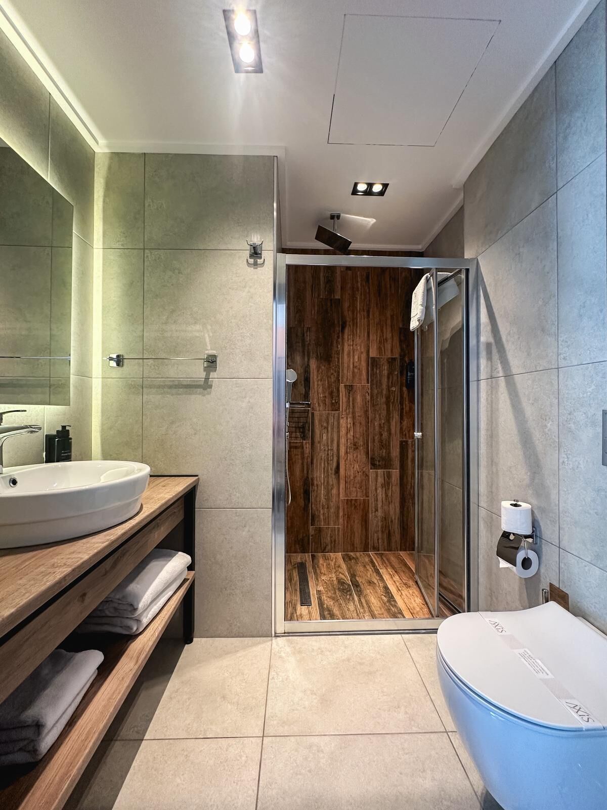 A modern bathroom with a glass shower enclosure, a white sink, and a blue bathtub.