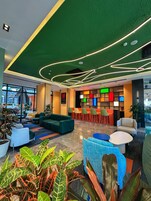 Un lobby moderno con techo verde, zonas de estar y un bar de decoración colorida.
