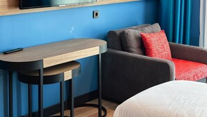 A hotel room with a bed, a desk with a chair, a sofa, a TV mounted on the wall, and a window with curtains. - Axis Hotel (Trabzon)