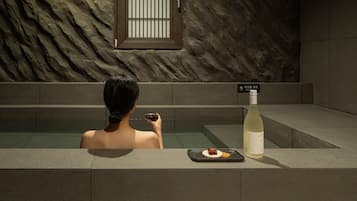 Une personne dans une baignoire, avec une bouteille de vin blanc et un plateau contenant un dessert.