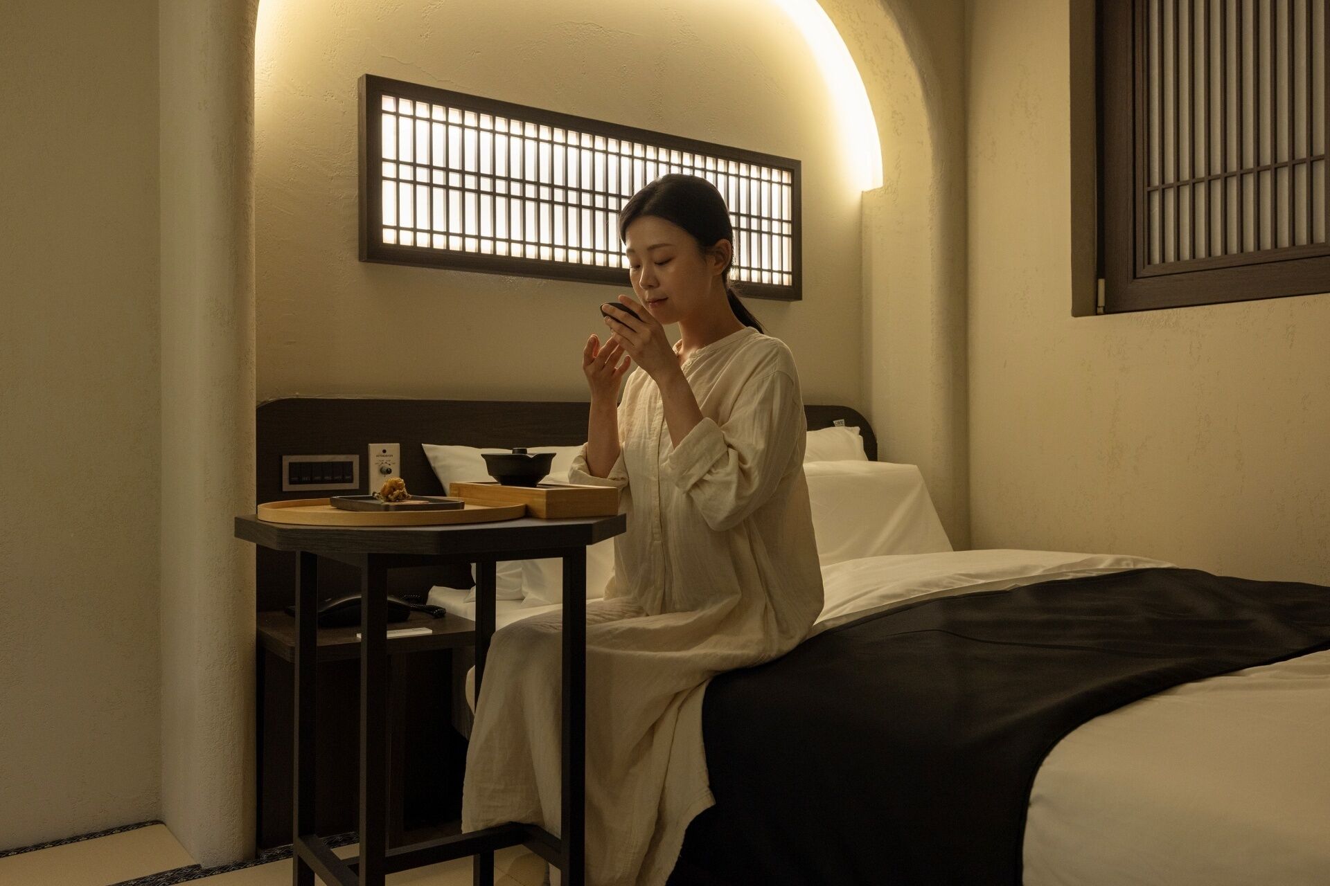A hotel room with a bed, bedside table, and a wall-mounted light fixture.