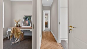 A hallway with a wooden floor, a white door with a gold handle, and a framed artwork on a shelf. - Belle Grove (Cape Town)