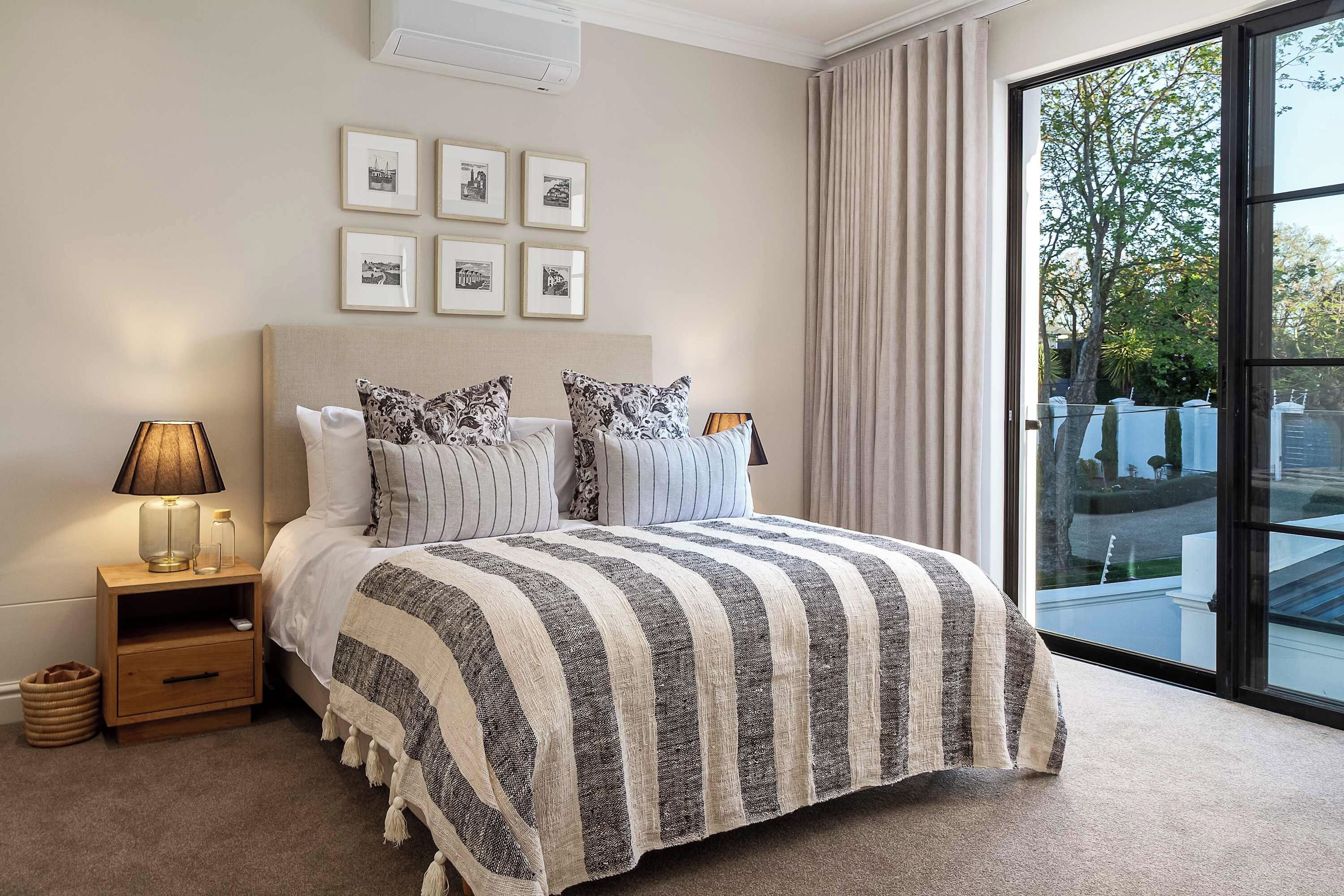 A bedroom with a large bed, a nightstand with a lamp, a window with curtains, and framed pictures on the wall.