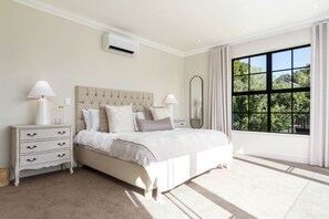 Ein Schlafzimmer mit einem großen Bett, Nachttischen, einer Klimaanlage, einem Spiegel und einem Fenster mit Blick auf Bäume.
