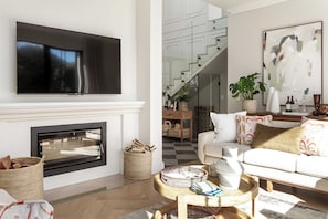 A modern living room with a fireplace, a flat-screen TV, a staircase, and a large abstract painting. - Belle Grove (Cape Town)