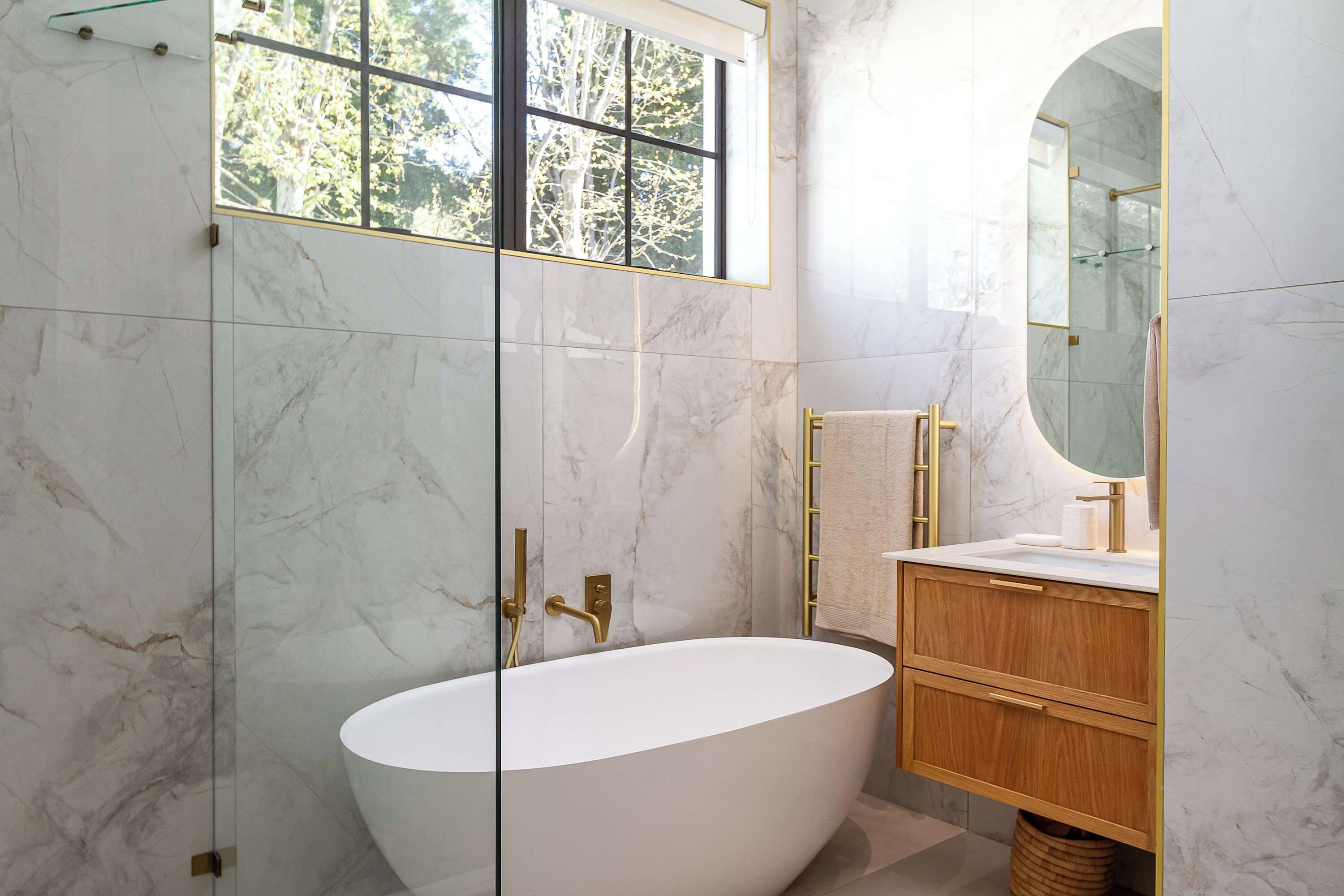 Une salle de bain moderne avec une baignoire sur pieds, un meuble-lavabo avec un miroir et une fenêtre donnant sur la verdure.