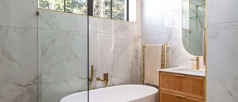 A modern bathroom with a freestanding bathtub, a vanity with a mirror, and a window with a view of trees.