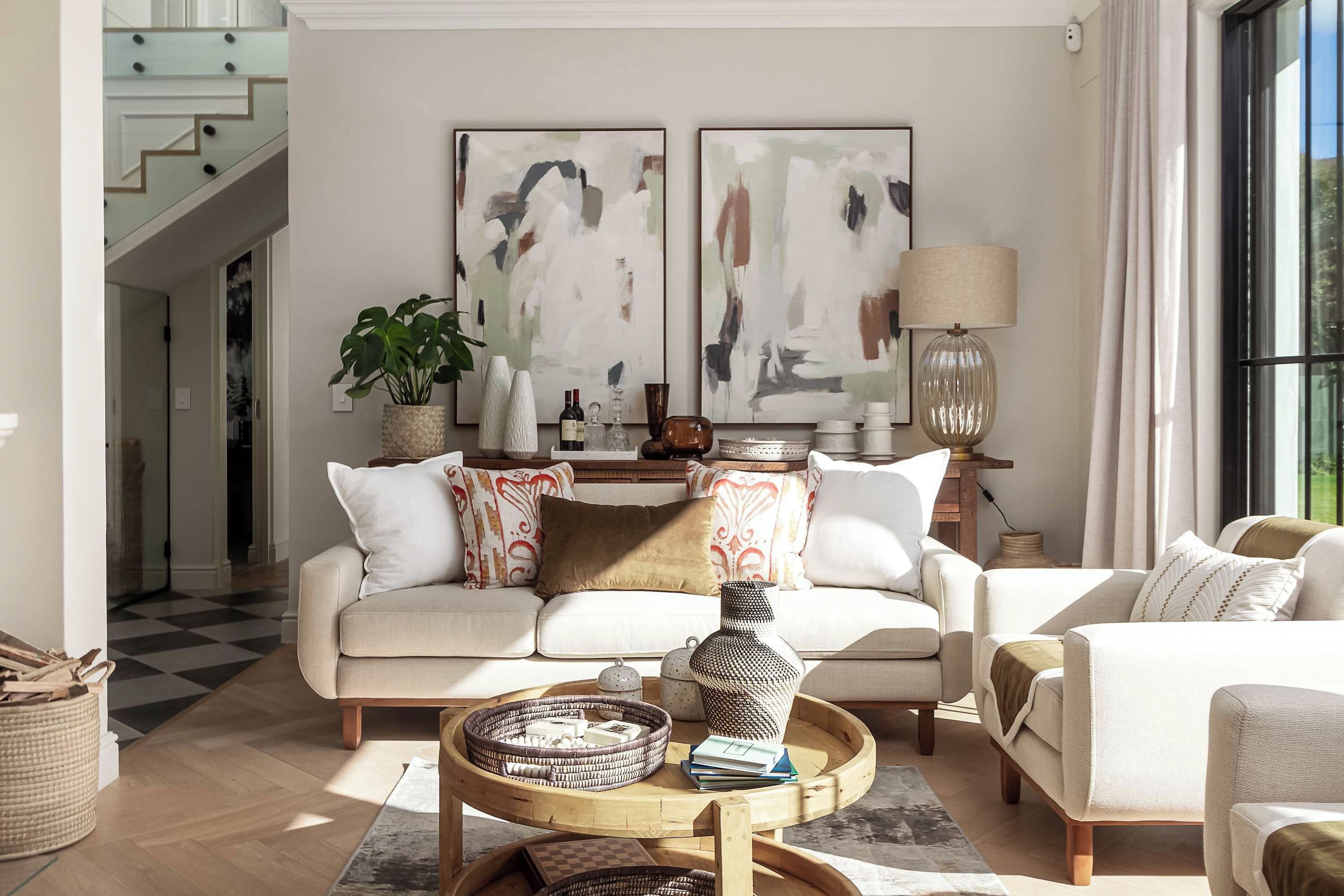 Uma sala de estar moderna com sofá, poltronas, mesa de centro e quadros abstratos na parede.