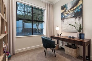 A room with a large window, a desk with a lamp, a chair, a bookshelf, and a painting on the wall. - Belle Grove (Cape Town)