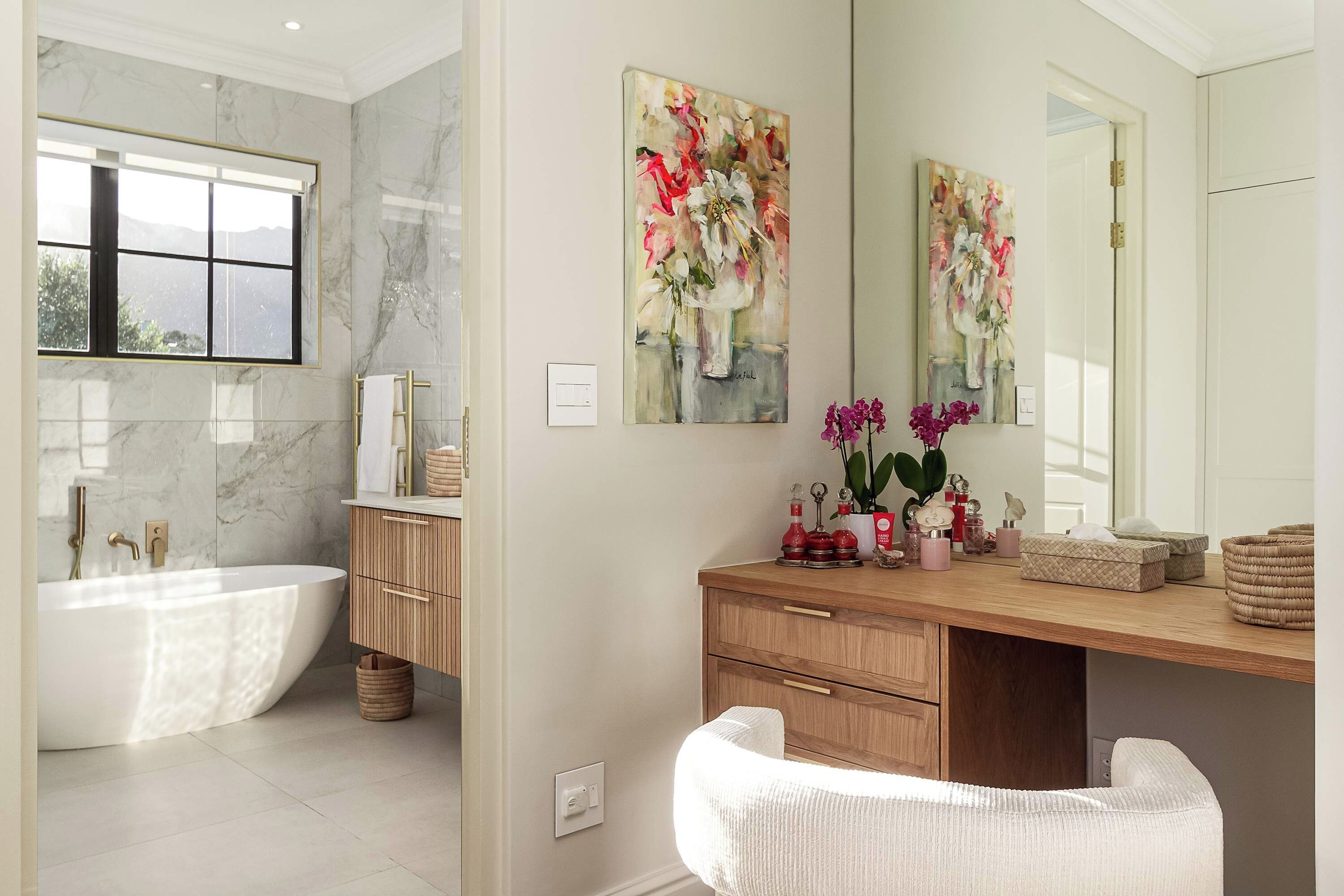 A modern bathroom with a freestanding bathtub, a vanity with a mirror, and two floral paintings on the wall.