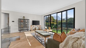 A spacious living area with a large window, a television, and a bookshelf. - Belle Grove (Cape Town)