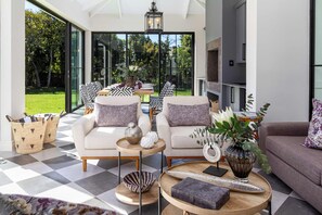 A modern living room with a checkered floor, two sofas with patterned cushions, a coffee table with decorative items, and a view of a garden through large windows. - Belle Grove (Cape Town)