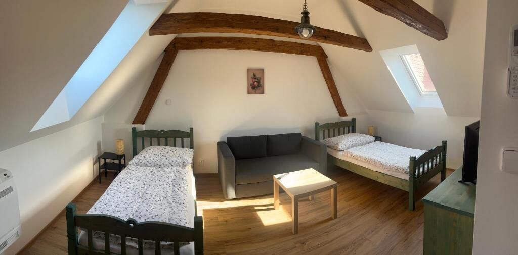 A room with a sloped ceiling, two beds, a sofa, a table, and a window.