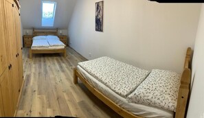 A bedroom with two beds, a wooden wardrobe, a skylight, and a painting on the wall.
