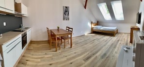 A compact room with a kitchenette, a dining table with chairs, a bed, and skylights.