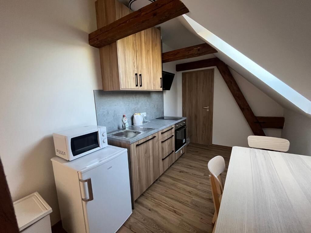 A compact kitchen with wooden cabinets, a microwave, a sink, and a small refrigerator.